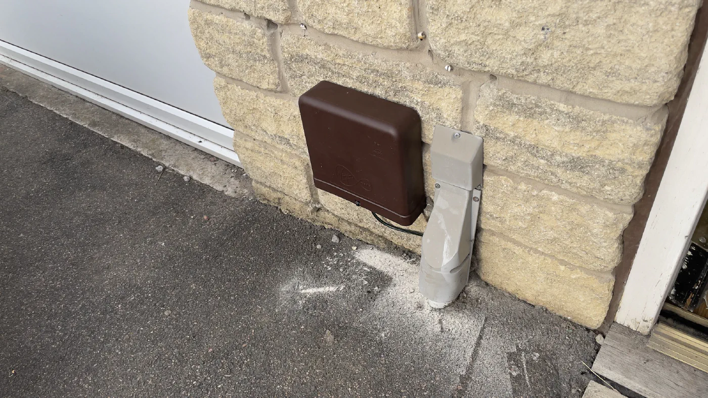 A brown Virgin Media termination box newly fitted to the stone exterior wall of the house, next to a grey duct running down to the ground