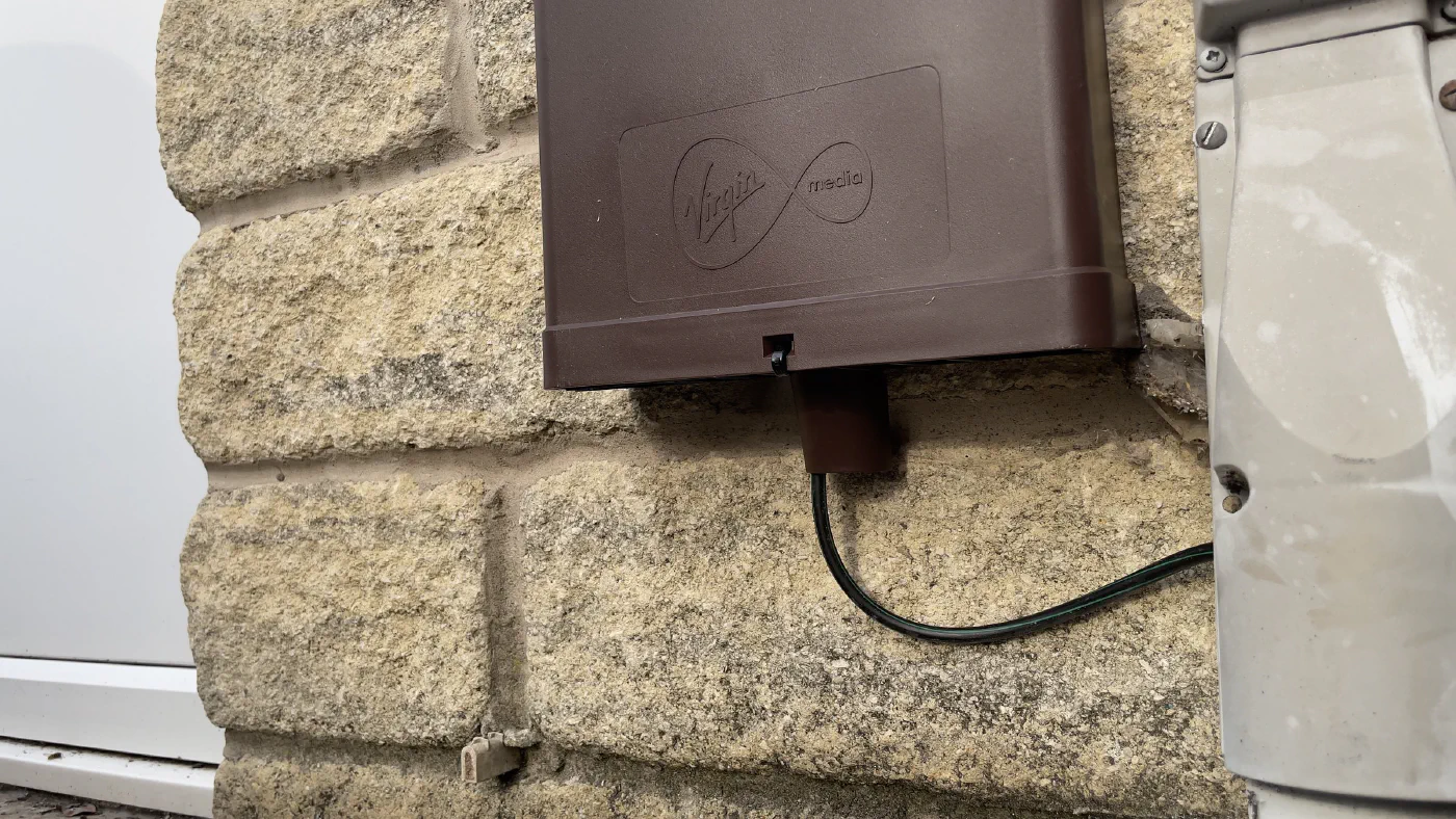 Close-up of the brown Virgin Media external box, embossed with the Virgin Media logo, with the fibre cable entering from below